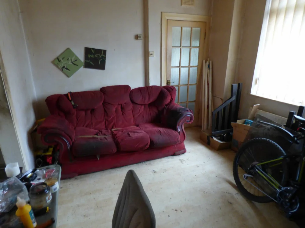 A tired living room with a worn sofa and bare floorboards in a house in disrepair