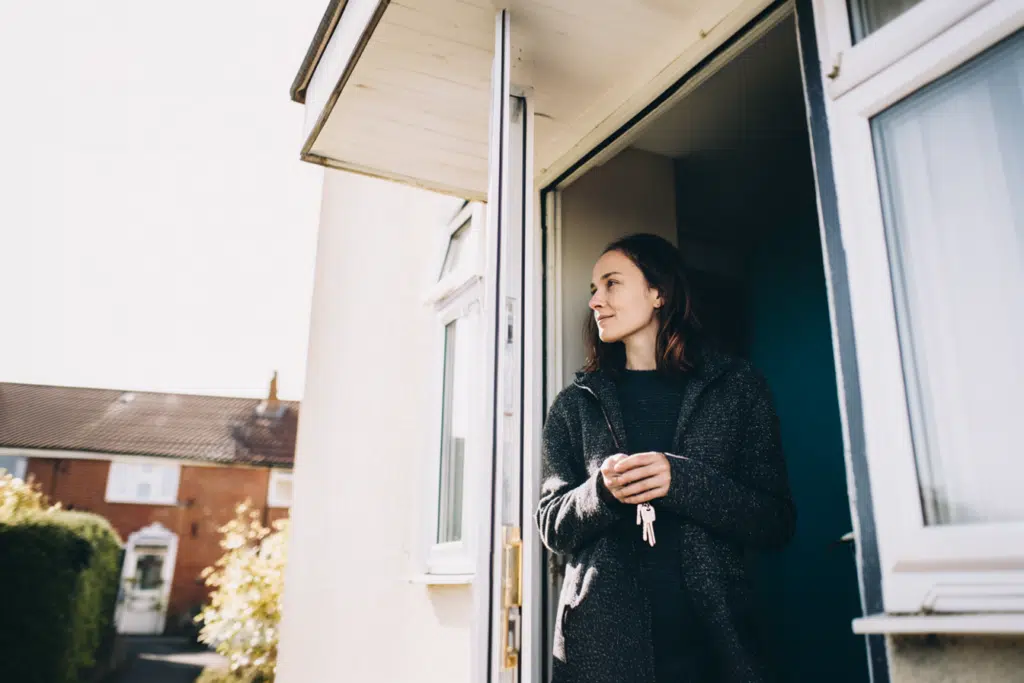A woman standing at the front door of her home, ready to sell